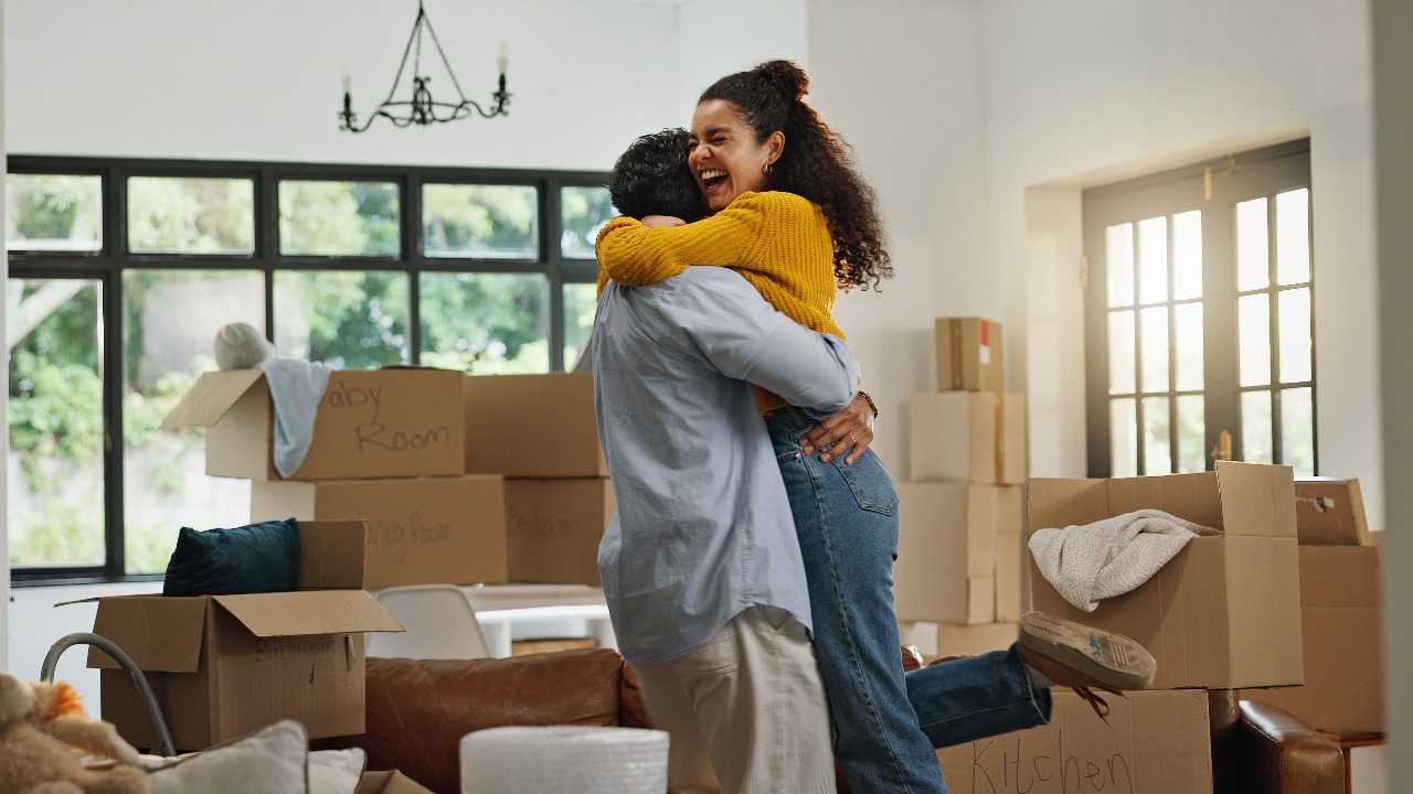 Happy couple hugging among packed boxes in their new home, celebrating a successful move while moving interstate to a new location.